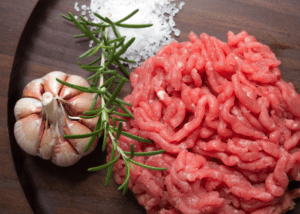 Fresh ground meat with garlic and rosemary on a wooden surface.