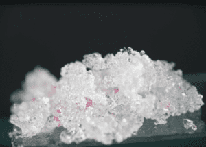 Close-up of crystalline ice with pink reflections on a dark background.