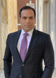 Man in a dark pinstripe suit and purple tie posing indoors.
