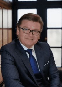 A man in a suit and glasses smiling.