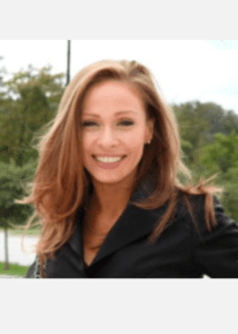 Smiling woman with long hair outdoors in a black jacket.