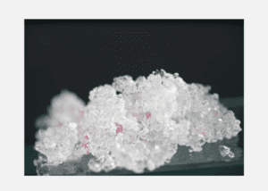 Close-up of crystalline salt with pink mineral inclusions on a dark background.
