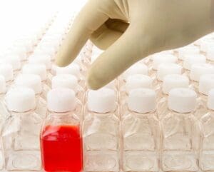 Hand selecting a red liquid sample from multiple clear samples in a lab.