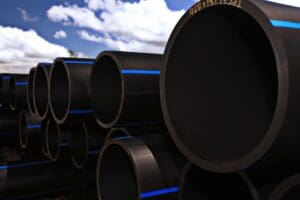 Stacked large black pipes against a blue sky with clouds.