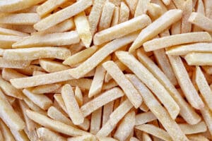 Close-up of uncooked frozen French fries piled together.