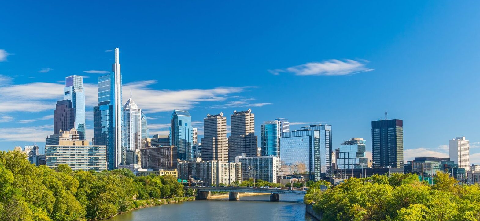 City skyline with modern skyscrapers and a river under a blue sky.