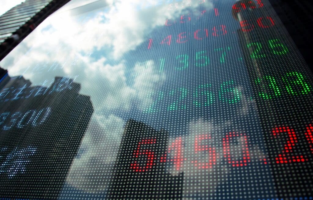 Digital stock display reflecting buildings and clouds.