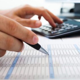 Hands with pen and calculator reviewing spreadsheet